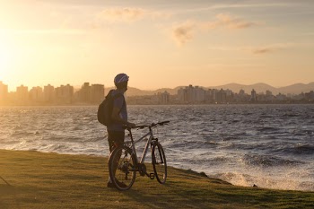 Man With Bicycle Standing on Cliff Front of Water Waves Golden Hour Photography