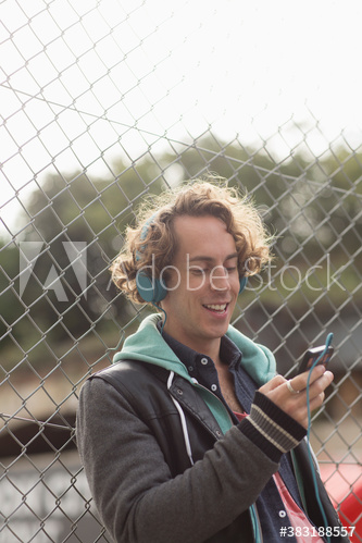 Man with headphones and smart phone listening to music at fence
