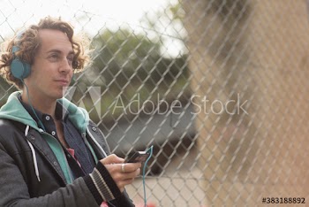 Man with headphones listening to music at chainlink fence