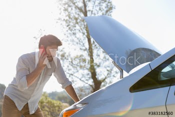 Man with smart phone calling for help and looking at car engine