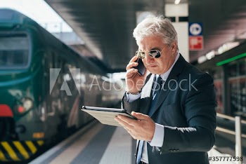 Mature businessman using smartphone and digital tablet at train station