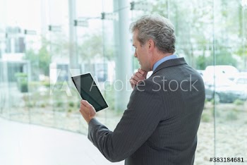 Mature corporate businessman using digital tablet at office window