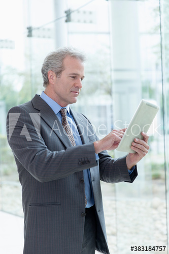 Mature corporate businessman using digital tablet at office window
