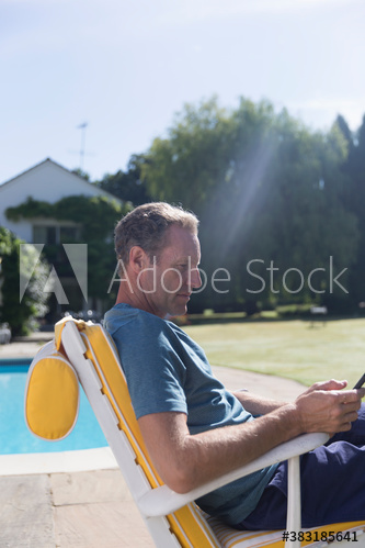 Mature man using smart phone at sunny poolside