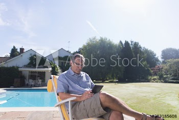 Mature man with digital tablet relaxing at sunny poolside