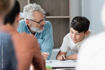 Mature teacher looking at asian schoolboy with notebook