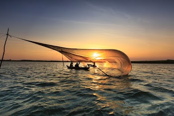 Men On Boat Catching Fish With Net During Golden Hour