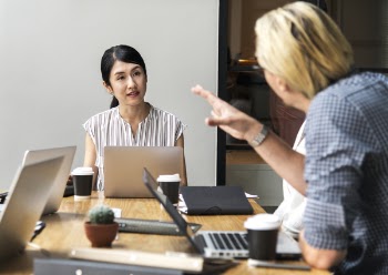 Men Talking to a Woman Sitting in Front of Silver Laptop Computer