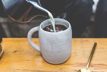 Milk Poured on Coffee on Brown Wooden Table