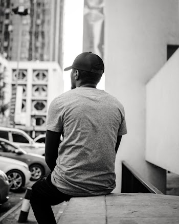 Monochrome Photo of Man Sitting On Ledge