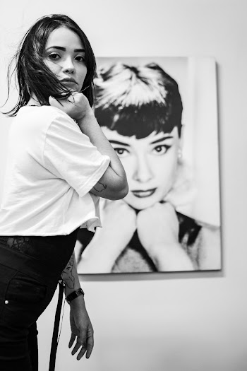 Monochrome Photo of Woman Standing Near Audrey Hepburn Painting