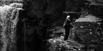 Monochrome Photography of Person Standing Near Rock Formation