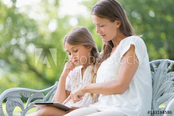 Mother and daughter using digital tablet on bench in garden