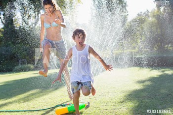 Mother and son running through sprinkler in summer backyard