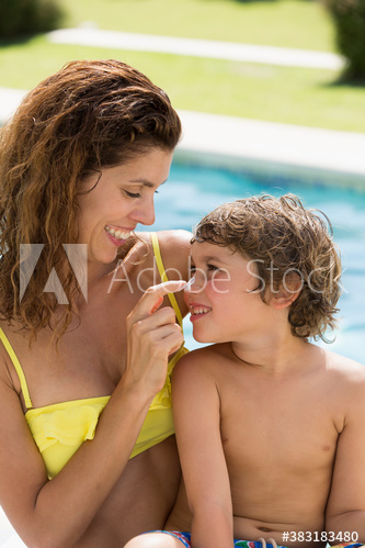 Mother applying sunscreen to nose of son at sunny poolside