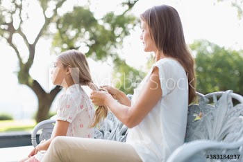Mother braiding hair of daughter on bench in sunny garden