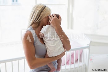 Mother cuddling baby daughter in baby nursery