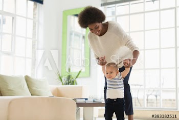 Mother helping cute baby son learn to walk in living room