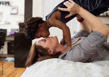 Mother kissing her daughter while lying on bed at home