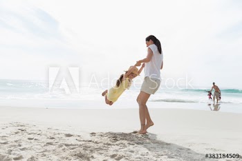 Mother swinging daughter on sunny ocean beach
