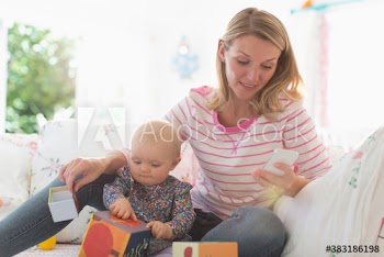Mother using smart phone and watching daughter playing with toys