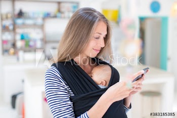 Mother with baby son in baby sling using smart phone