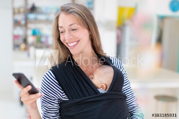 Mother with baby son in baby sling using smart phone