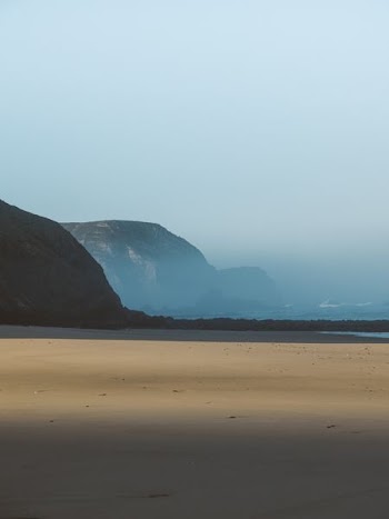 mountain covered with smoke beside body of water at daytime