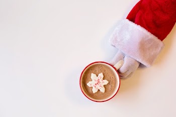 Mug of Chocolate Drink With Snowflake-Shaped Cookie On Top Held By A Person In Santa Suit