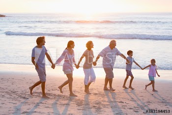 Multi-generation family holding hands and walking on sunny beach