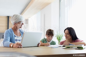 Multi-generation family using laptop and coloring at dining table