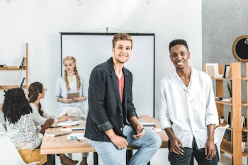 Multicultural smiling businessmen looking at camera and colleagues discussing work behind in office