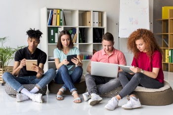 Multiracial friends studying with electronic gadgets and books sitting in study room Free Photo