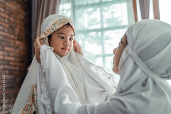 Muslim mother helps young daughter put on scarf before prayer