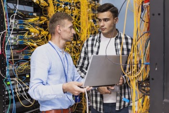 Network engineers working in a server room with a laptop Free Photo