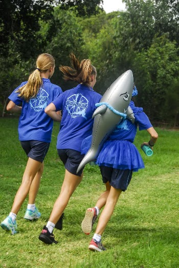 One Girl Carrying Shark Balloon Running With Two Girls in Blue Uniforms