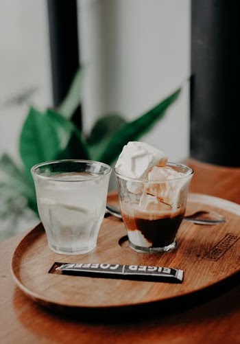 one glass filled with ice cream and one with clear water on brown wooden tray
