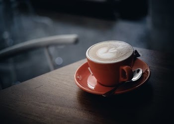 orange ceramic mug with saucer and coffee on it