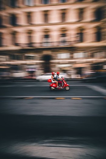 panning photography of two person riding red motor scooter