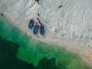 People and Three Blue Boats on Beach With Green Water Aerial Photography