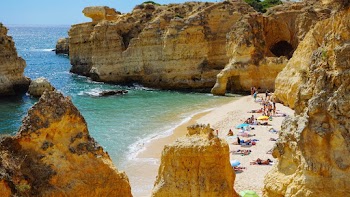 People in Beach Surrounded With Brown Cliffs