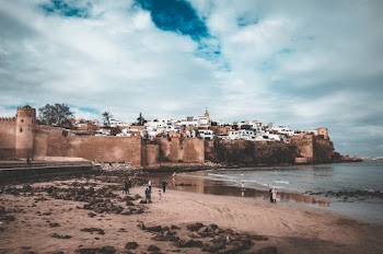 People On The Seashore Close To A Village Surrounded By Fortified Walls