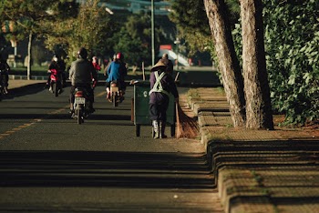 People Riding Motorcycles and Another Person Pushing Green Garbage Bin on Road