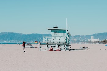 People Sitting on Sand Near White Wooden Cottage Near Seashore