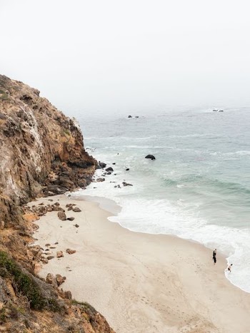 people standing at seashore near rock cliff during daytime