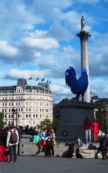 People Standing Below Rooster Statue by the Building