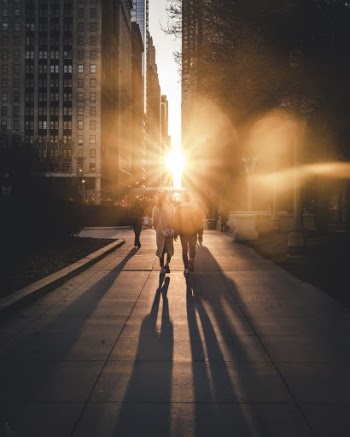 People Walking Down The Street With Ray Of Sun Between Two Buildings