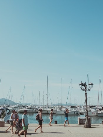 People Walking Near Boat Lot and Body of Water Under Blue Sky