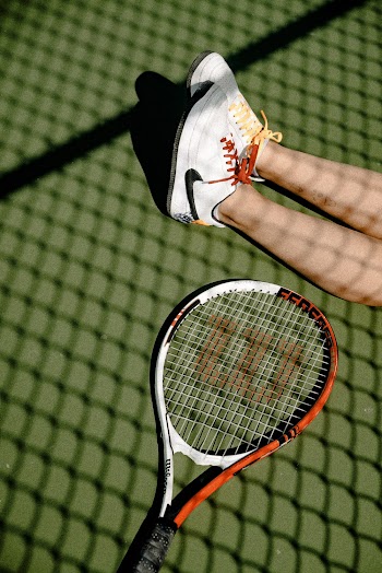 Person's Feet Wearing White-and-black Nike Low-top Sneakers Beside Lack White and Orange Wilsons Tennis Racket