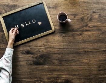 Person's Hand on Black Board With Hello Text Beside Brown Mug